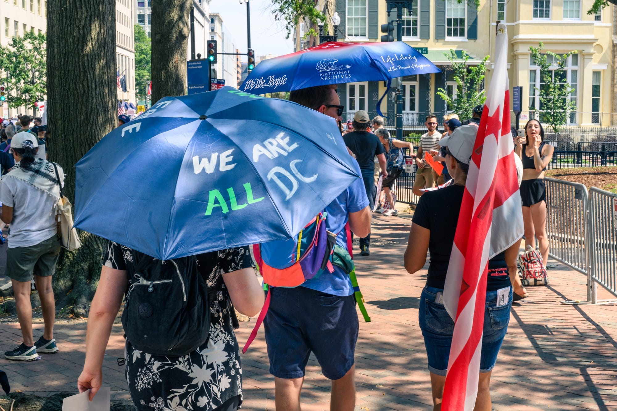 People walking, with one holding a large D.C. flag and another an umbrella that reads: "we are all D.C."