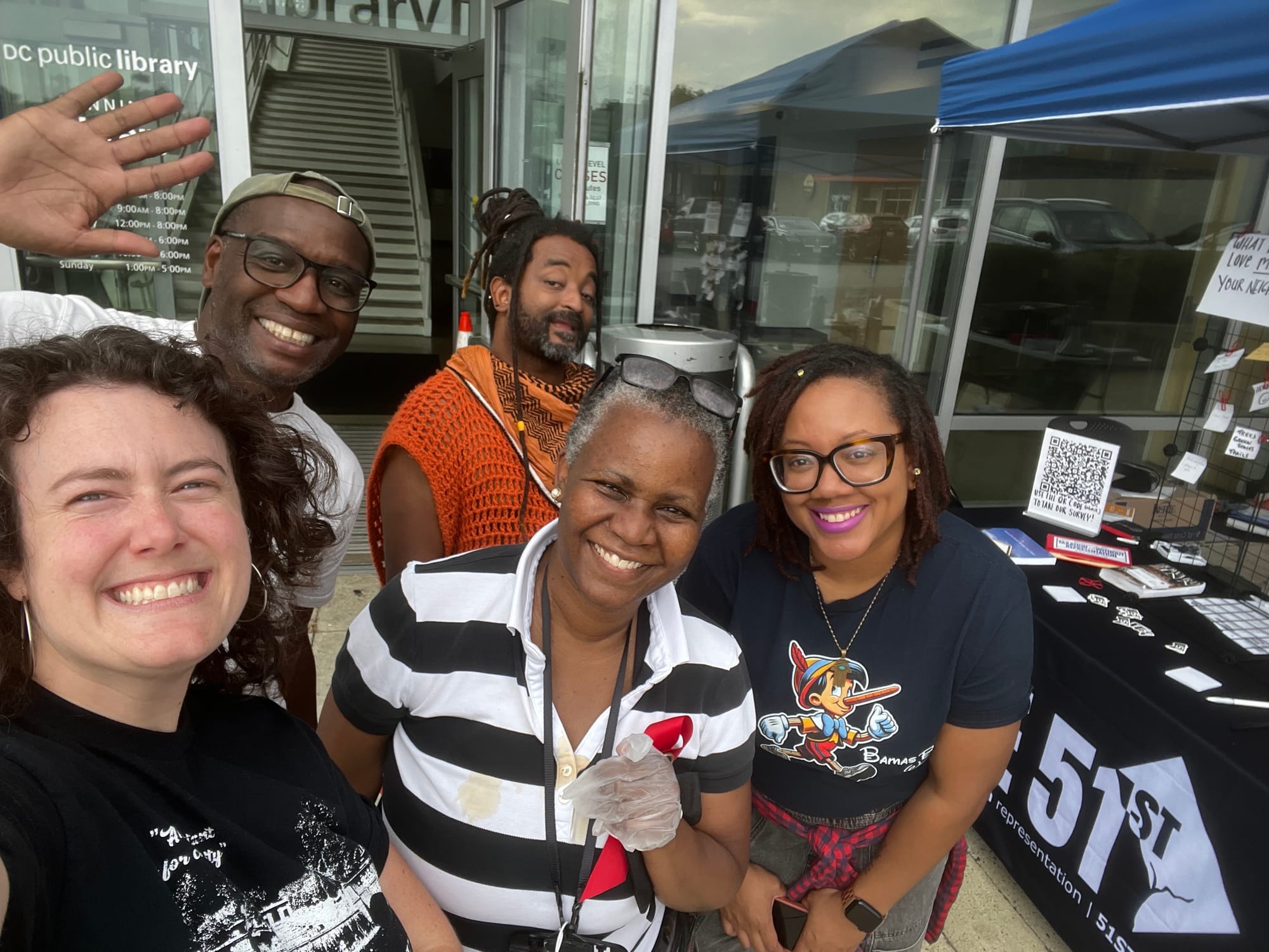 A selfie of five people in front of a table that reads The 51st