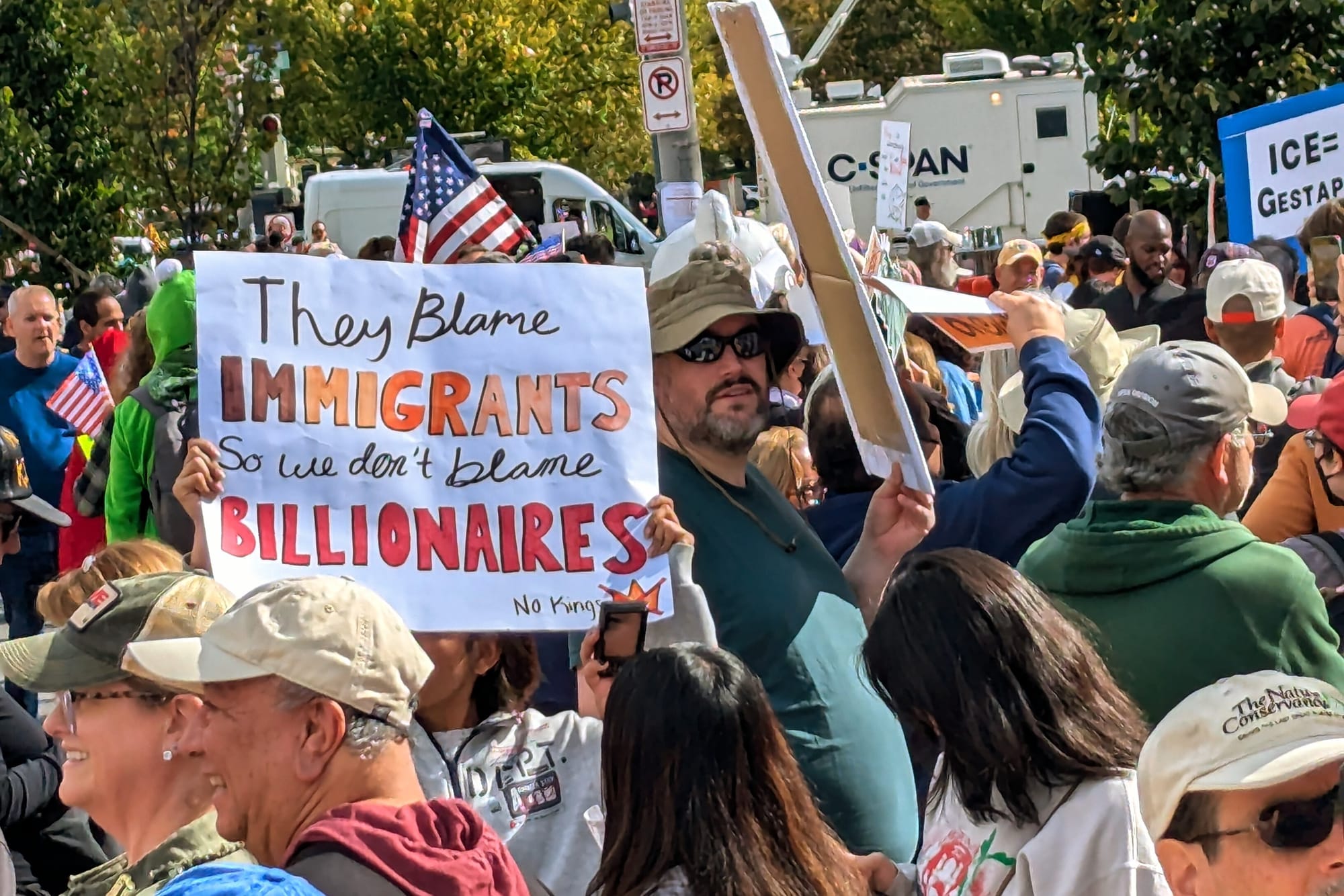 A sign at a protest reads "They blame immigrants so we don't blame billionaires."