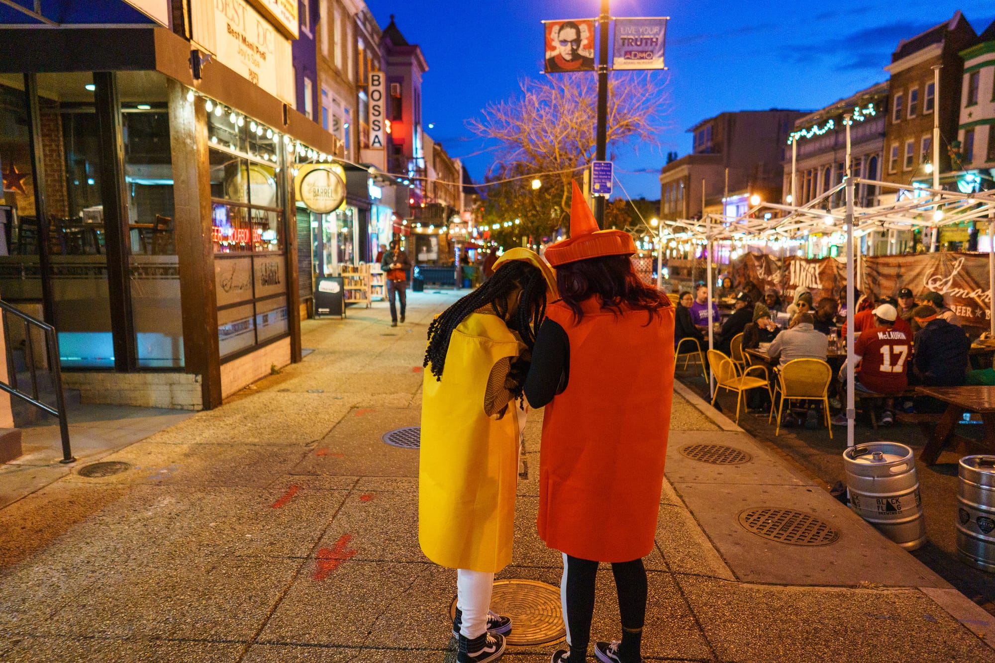 People dressed as mustard and ketchup bottles huddle on a D.C. sidewalk, next to a streatery.