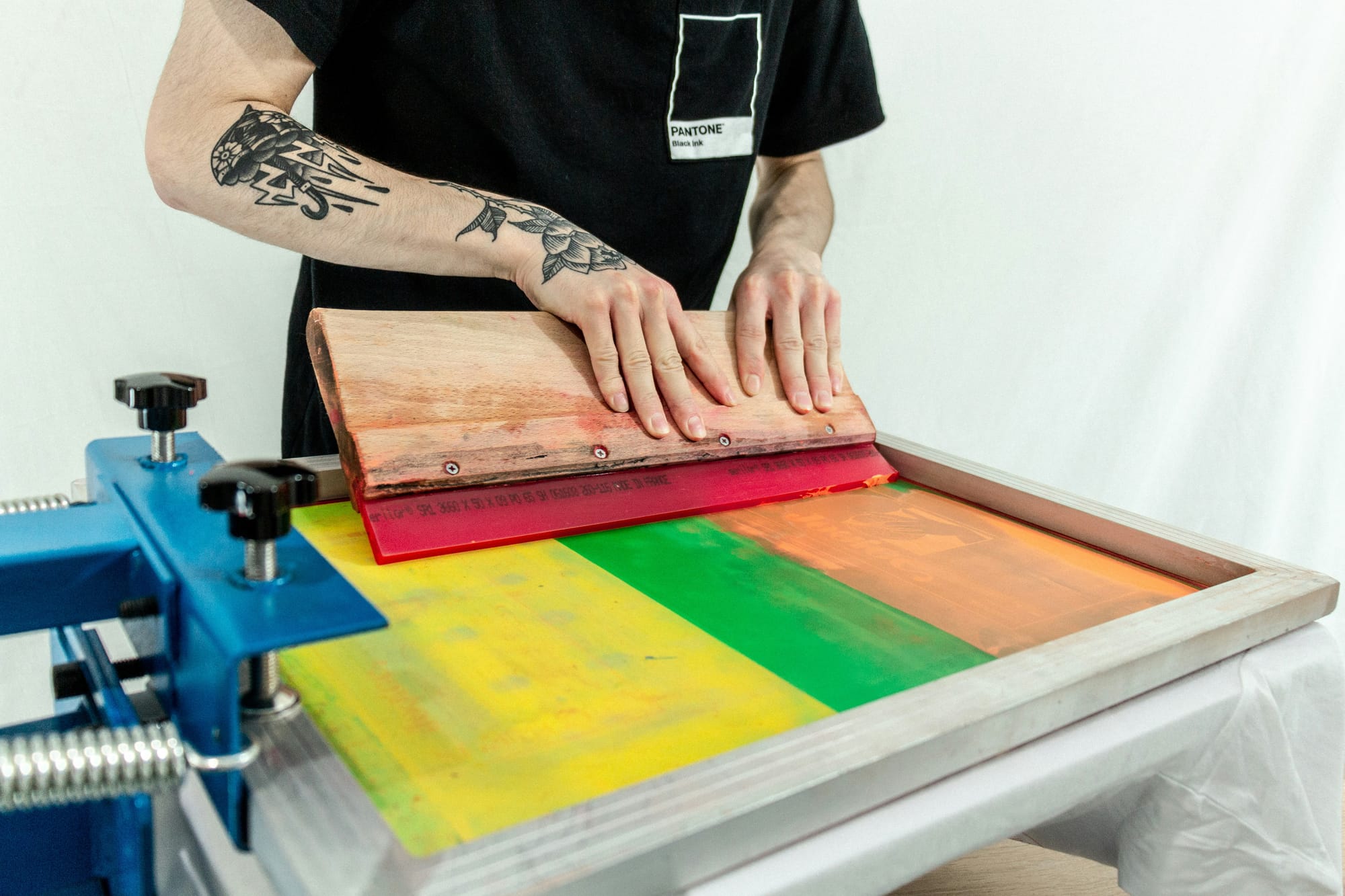 A person with tattoos screenprints in orange, green, and yellow.