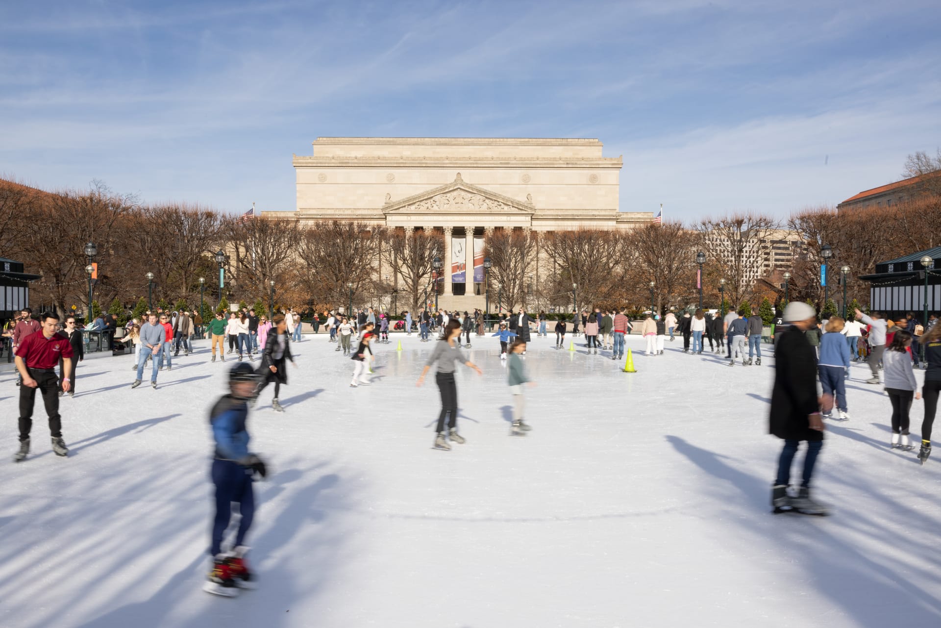 People ice skate on a rink with a museum in the background.