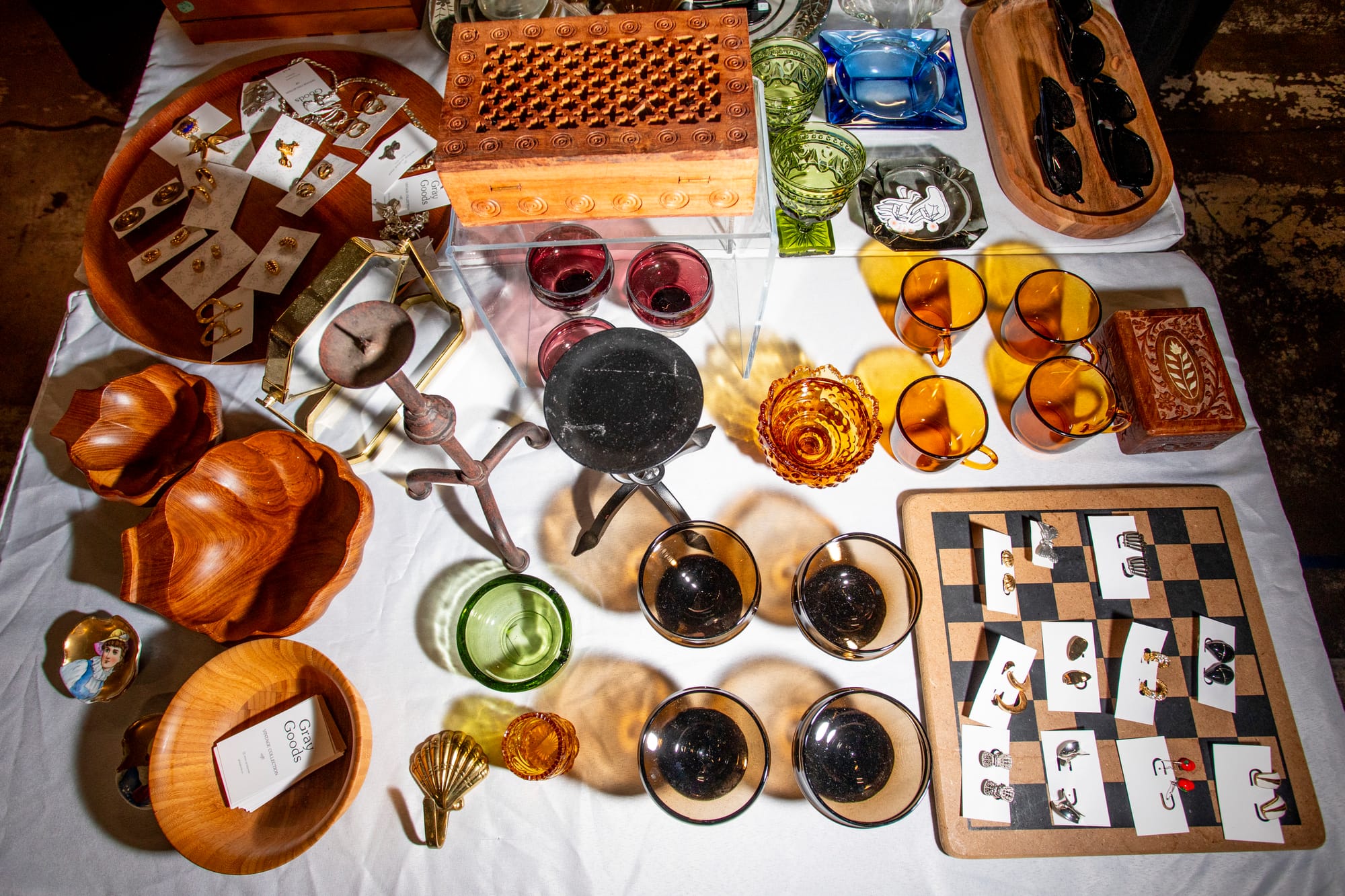 Two tables stacked with vintage knickknacks, glassware, wooden bowls, and jewelry for sale.