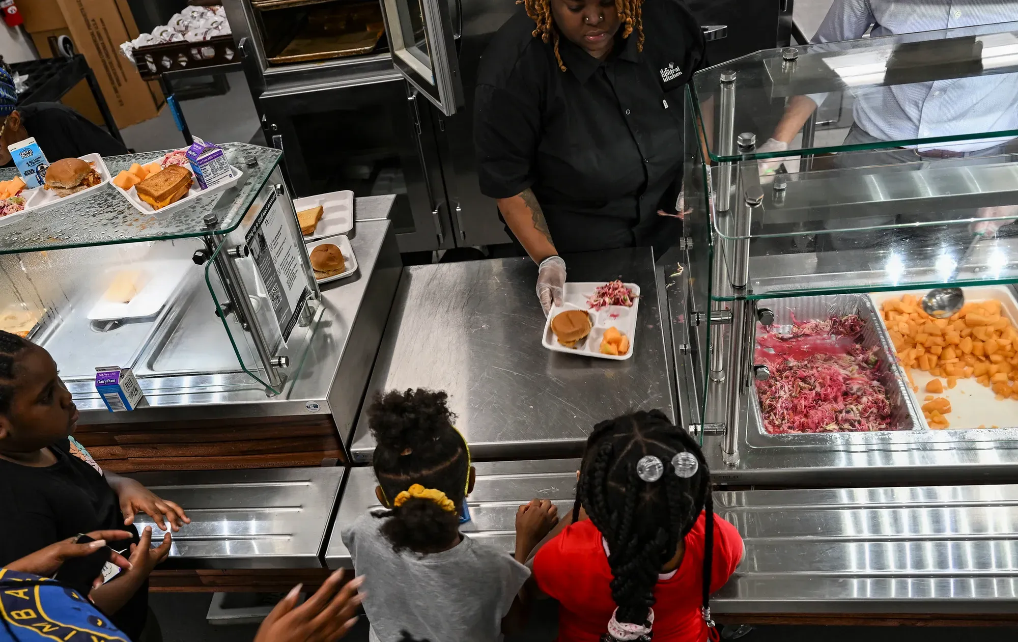 A school lunch worker passes a plate of food to children standing in line at a school cafeteria