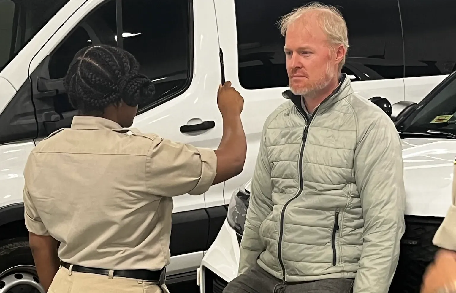 A police officer holds a pen in front of a man in a puffer jacket's eyes.