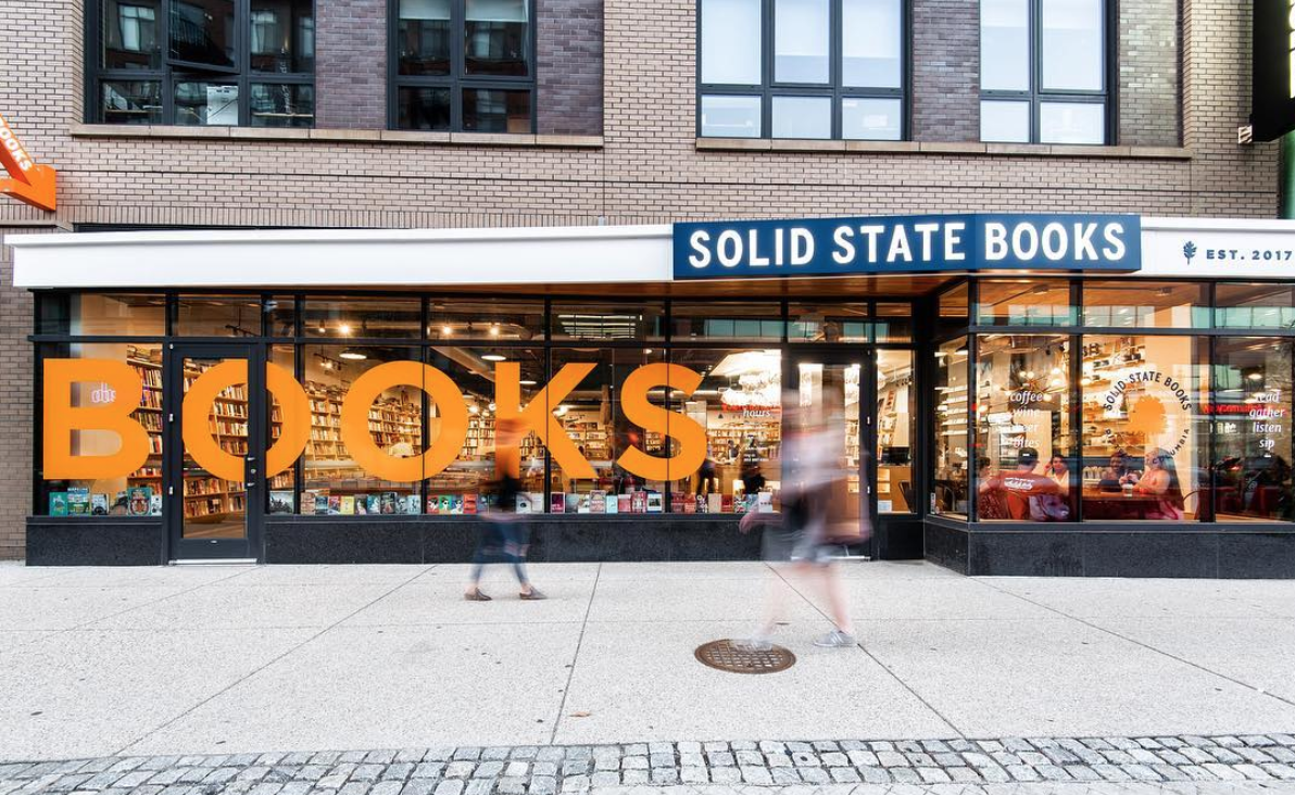 A picture of the exterior of Solid State Books, with blurred pedestrians walking by. 
