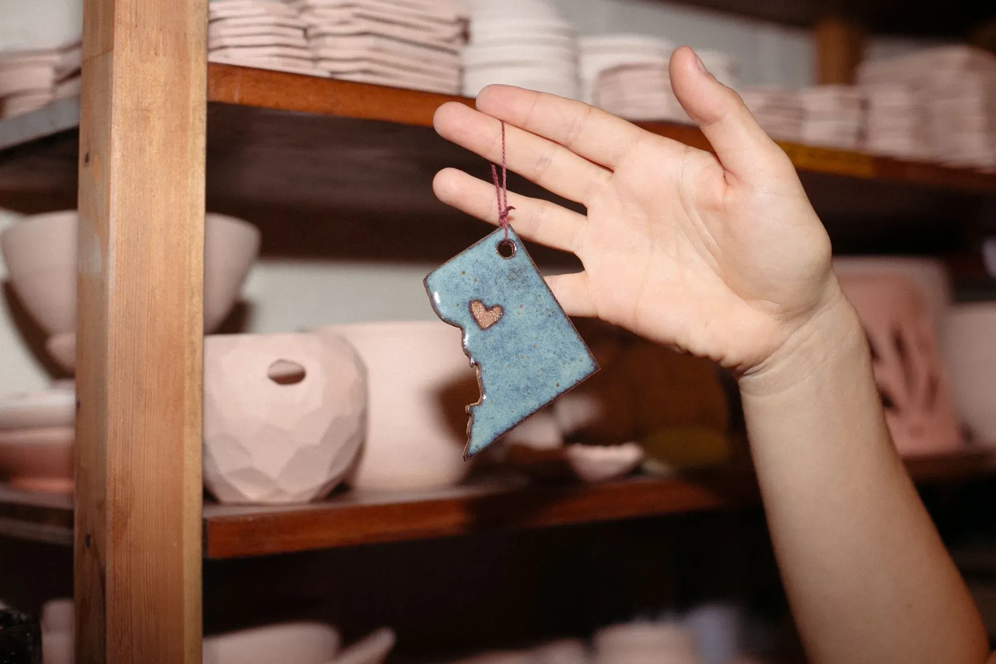 A hand holding a ceramic ornament in the shape of Washington D.C, with pottery in the background.