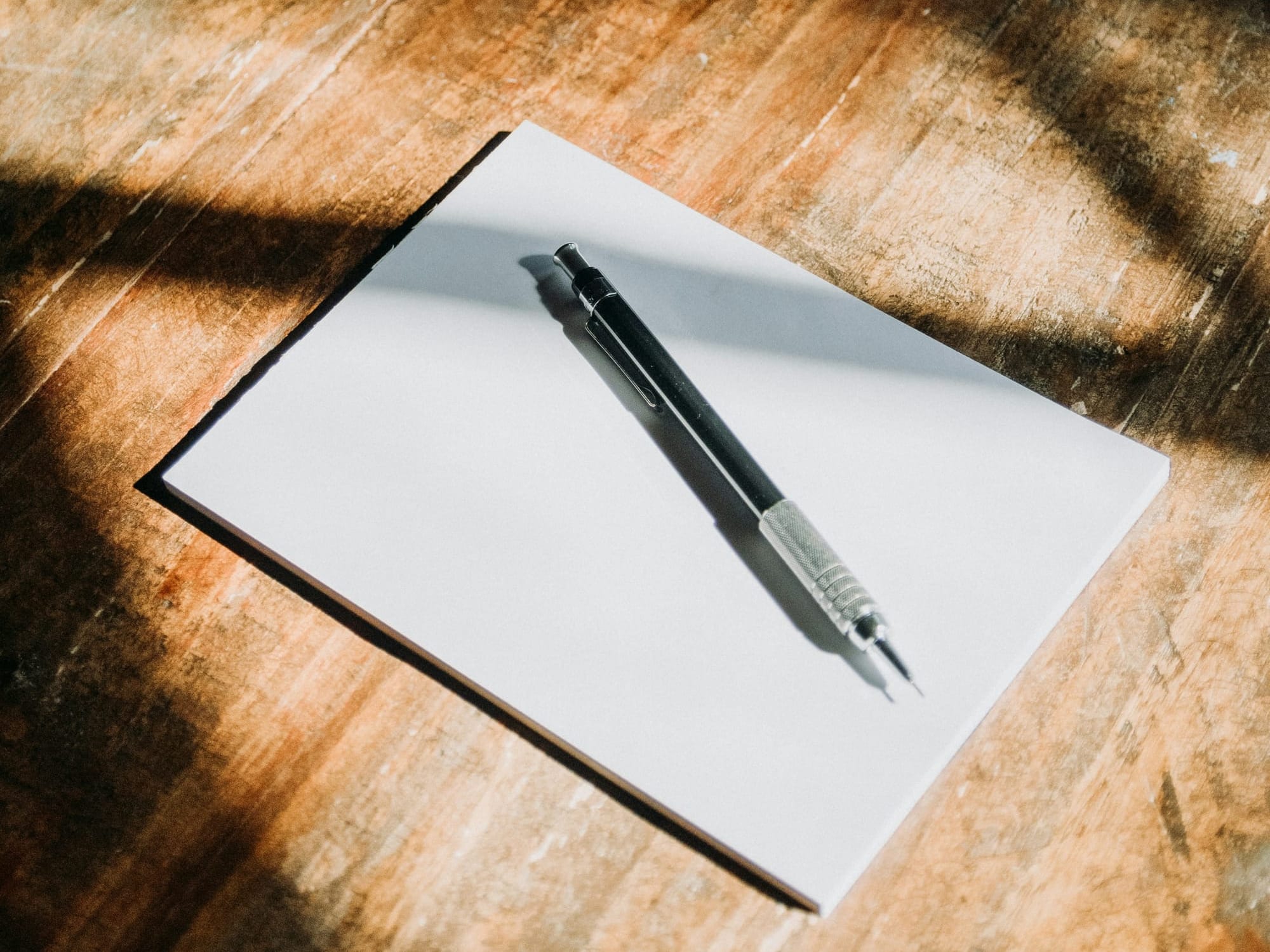 A pencil sits on a pad of paper on a wooden table.