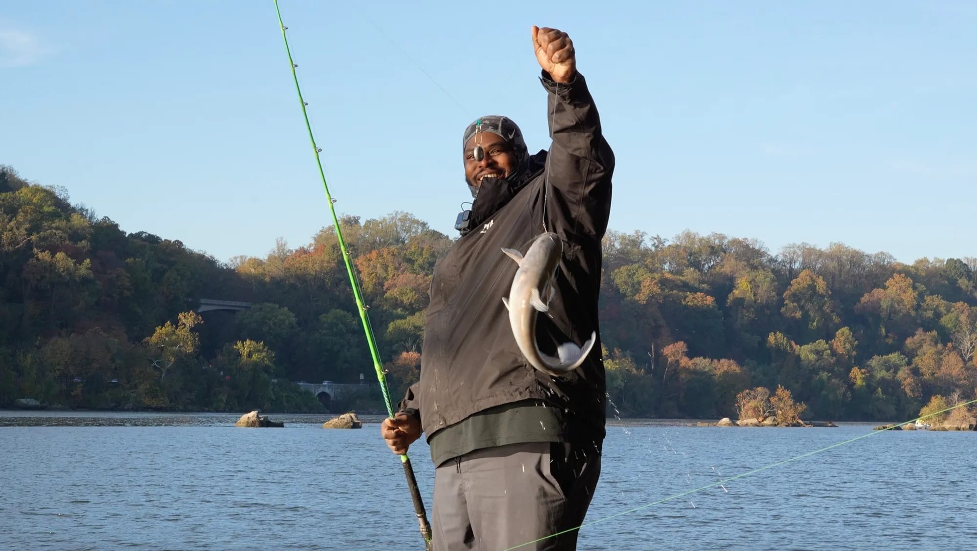 Ernest Robinson holding a flopping fish up to the camera with a smile, blue water in the background. 