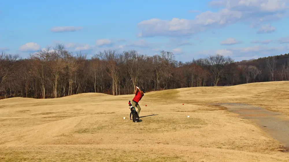Person in a red shirt gets ready to hit golf ball on open course. 