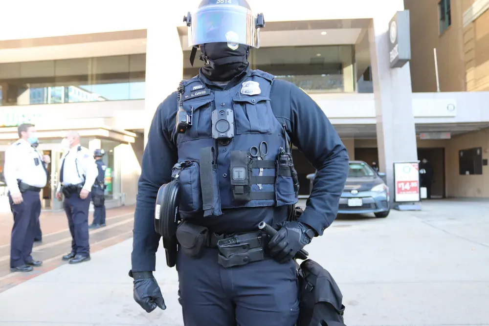 Masked officer in uniform stands in front of a building. 