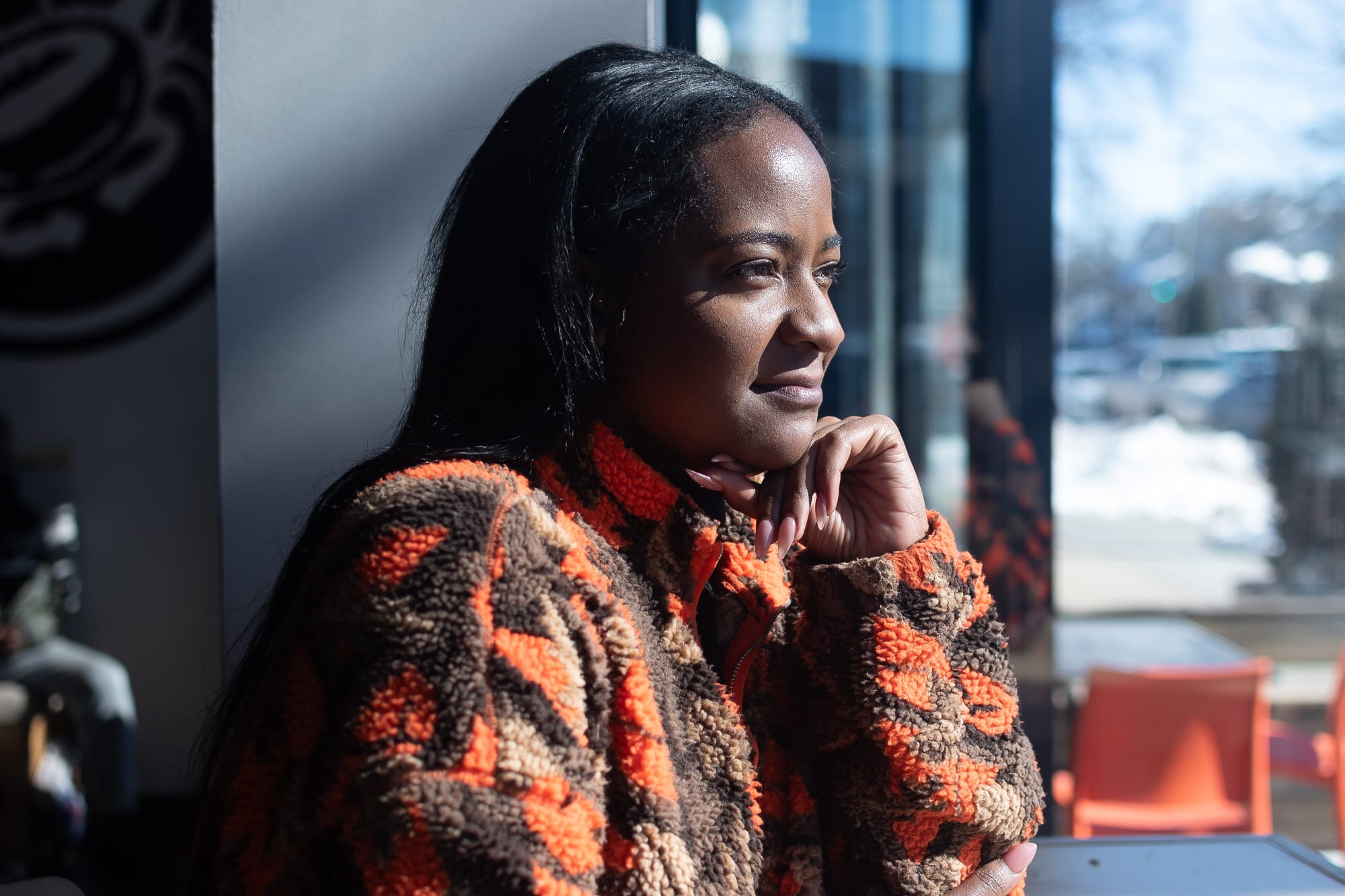 A photograph of a person with their hand on their chin, wearing an orange and brown fleece.