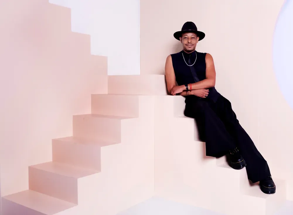 A photograph of a person dressed in all black sitting on a pink staircase.
