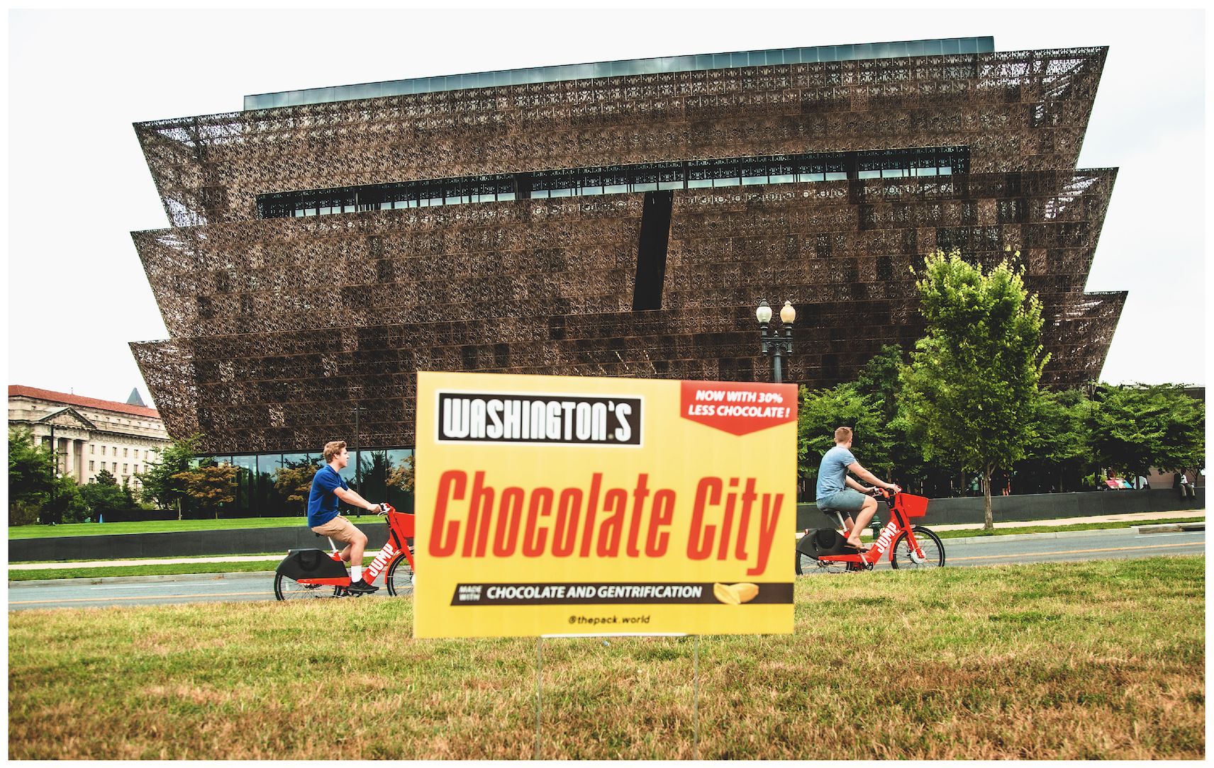 Two people ride rental JUMP e-bikes past a Chocolate City yard sign in front of D.C.'s National Museum of African American History and Culture.