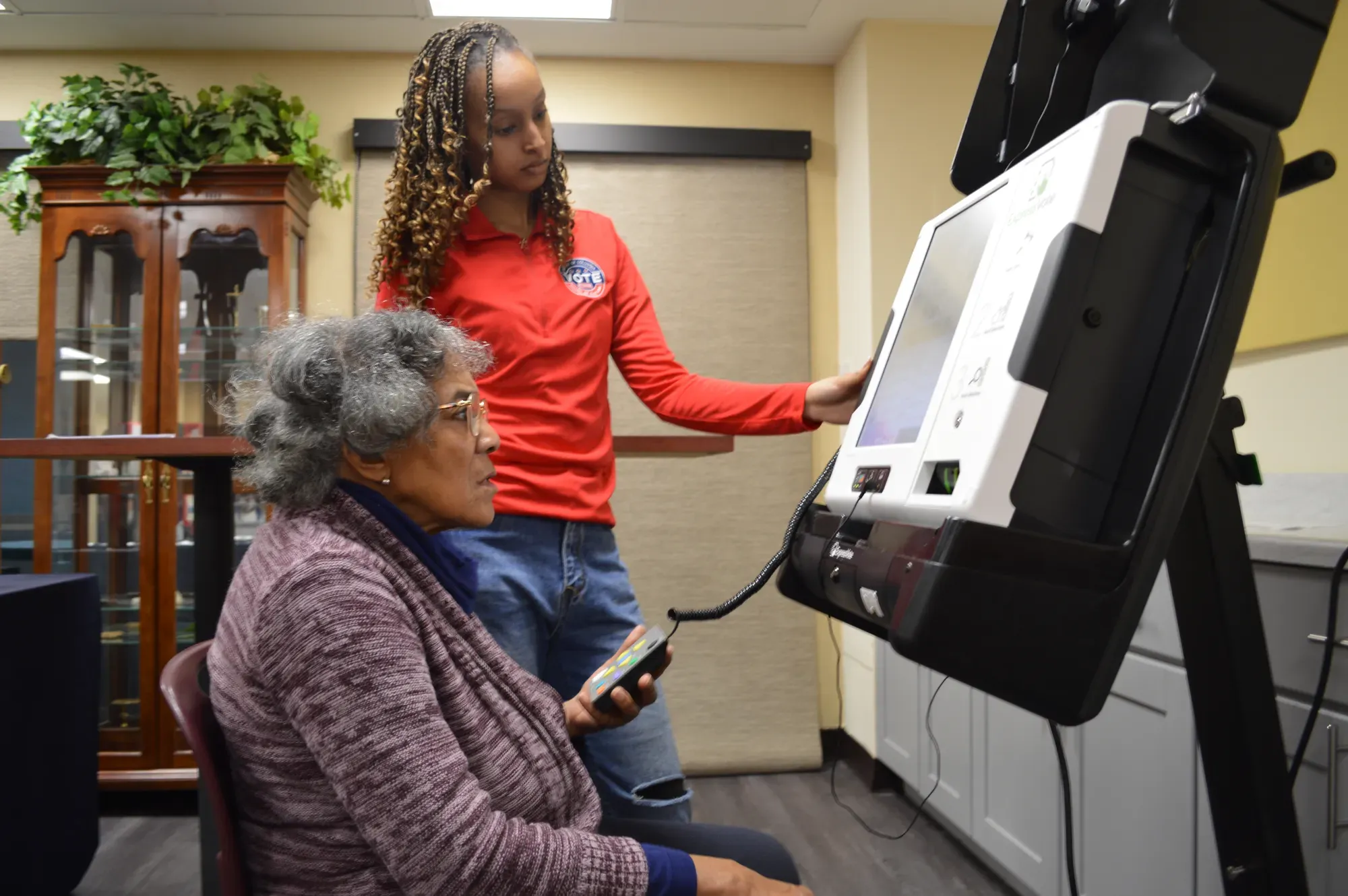 A person demonstrates to another person how to use a voting machine