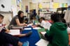 A teacher sits cross-legged on a colorful rug with a circle of students.