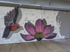 Mural featuring a hummingbird, flower, and shadow of a person, painted across two rollup doors.