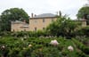 Photo of a light brown building in the back with green plants and flower garden in the forefront.