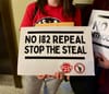 Person holding a sign that reads No I82 Repeal Stop The Steal