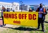 Two people holding a banner that reads Hands Off D.C.