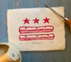 A print of the D.C. flag with sandwiches replacing the bars sits on a table next to tools.