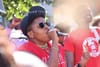 A person in a red shirt speaks into a microphone at a protest.