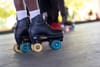 A closeup of a person's feet in black roller skates with blue and yellow wheels