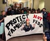 A group of protesters holds up a large banner that reads "Protect families not feds" and shows Muriel Bowser wearing an ICE vest.