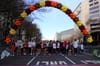 A crowd of runners lined up at a starting line, under a Thanksgiving-themed arch of balloons.