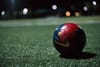 A blue and red soccer ball sitting on a pitch in the dark 