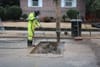 A person in a yellow suit leans over a hole in the concrete to update old gas pipes.
