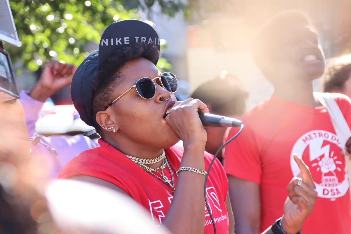 A person in a red shirt speaks into a microphone at a protest.