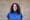 Maddie Poore, a white woman with curly black hair and a blue shirt, in front of a brick wall.