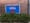 Blue yard sign saying 'This House Supports Federal Workers' against a brick wall with a green bush in front. 