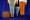 A suitcase and an umbrella stand between the bottom half of two people's bodies. 