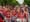 A group of women play drums in matching red, black, and white outfits that read Batalá.