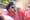 A person in a red shirt speaks into a microphone at a protest.