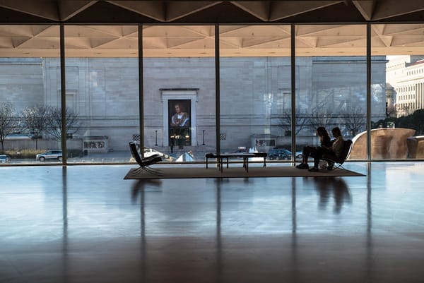 Two women sit in chairs before a wall of windows in the National Gallery of Art in D.C.