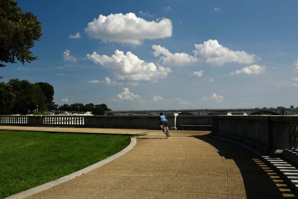 A cyclist in the middle of a bike path near the Potomac river on a sunny day with blue skies in the background.