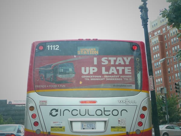 A picture of the back of a D.C. Circulator bus with a sign on the back that reads "I stay up late."