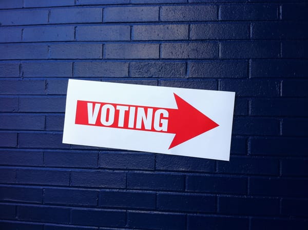 A red and white voting sign on a blue wall.