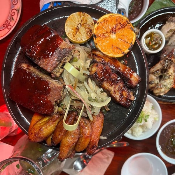 A close up of a plate filled with pork and plantains and garnished with lime and orange slices