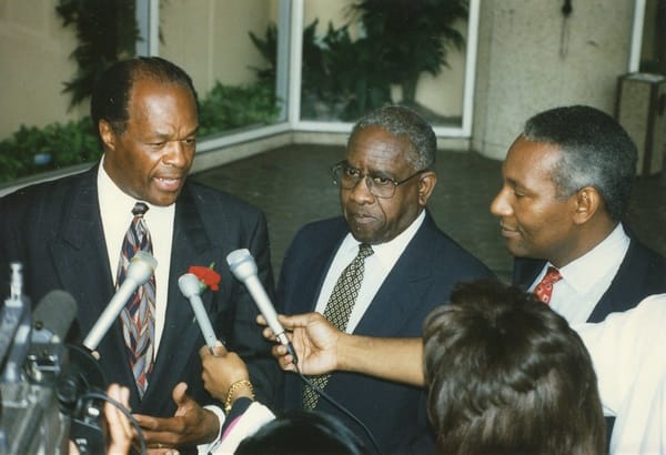 Marion Barry, an African American man, is standing beside reporters holding microphones to his face.