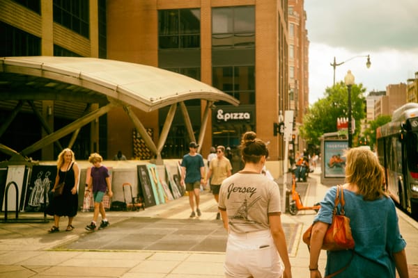 Groups of two people walk down Washington D.C.'s U Street with an art sale on the street in the background.