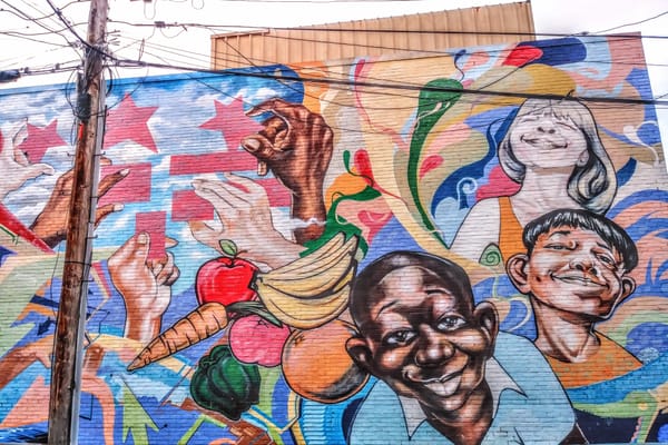 The mural depicts at least five hands placing pieces of the D.C. flag together, along with swirling colors, fresh produce, an