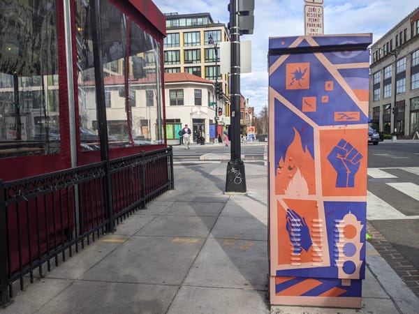 A picture of a sidewalk in D.C. with a small mural featuring fire, a first, and a traffic light. 