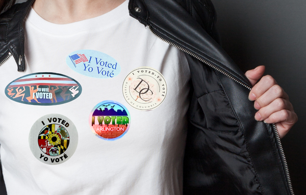 A photo of a woman in a white t-shirt with images of different "I voted" stickers on it.