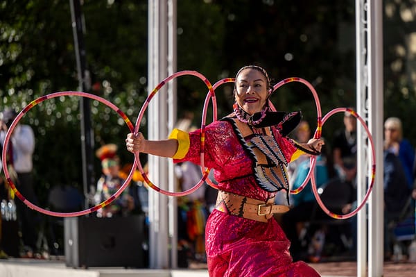 Woman in red attire balances five hula hoops in an outdoor performance.