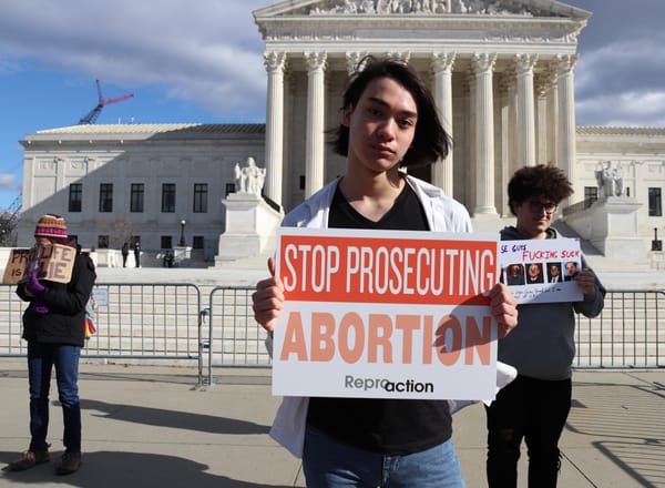 Three protesters in front of the Supreme Court, one holding a sign that reads: "Stop Prosecuting Abortion." 