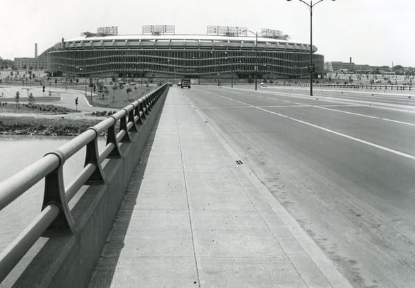 Black and white photo of a bridge leading to a large stadium.